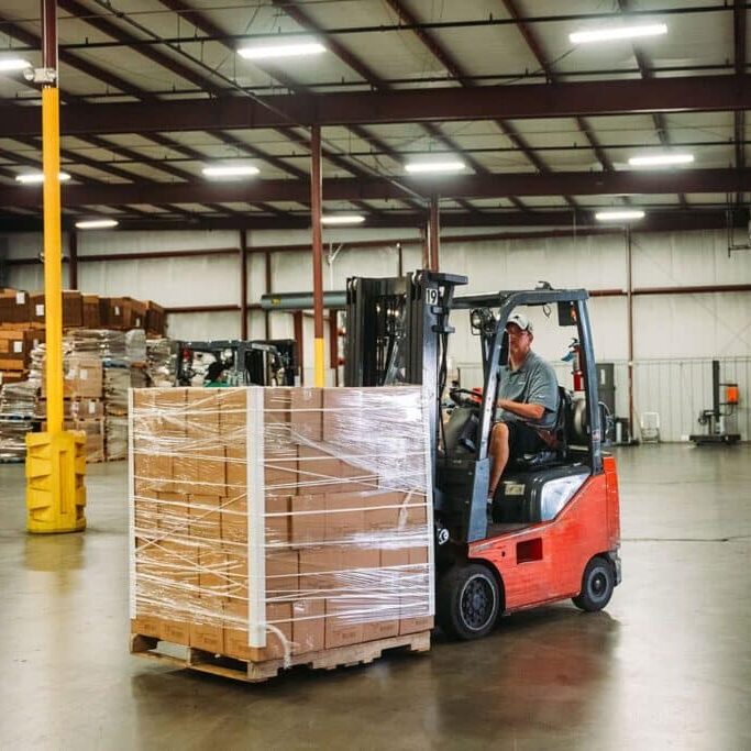 fork lift operator with cardboard boxes on a pallet in a warehouse